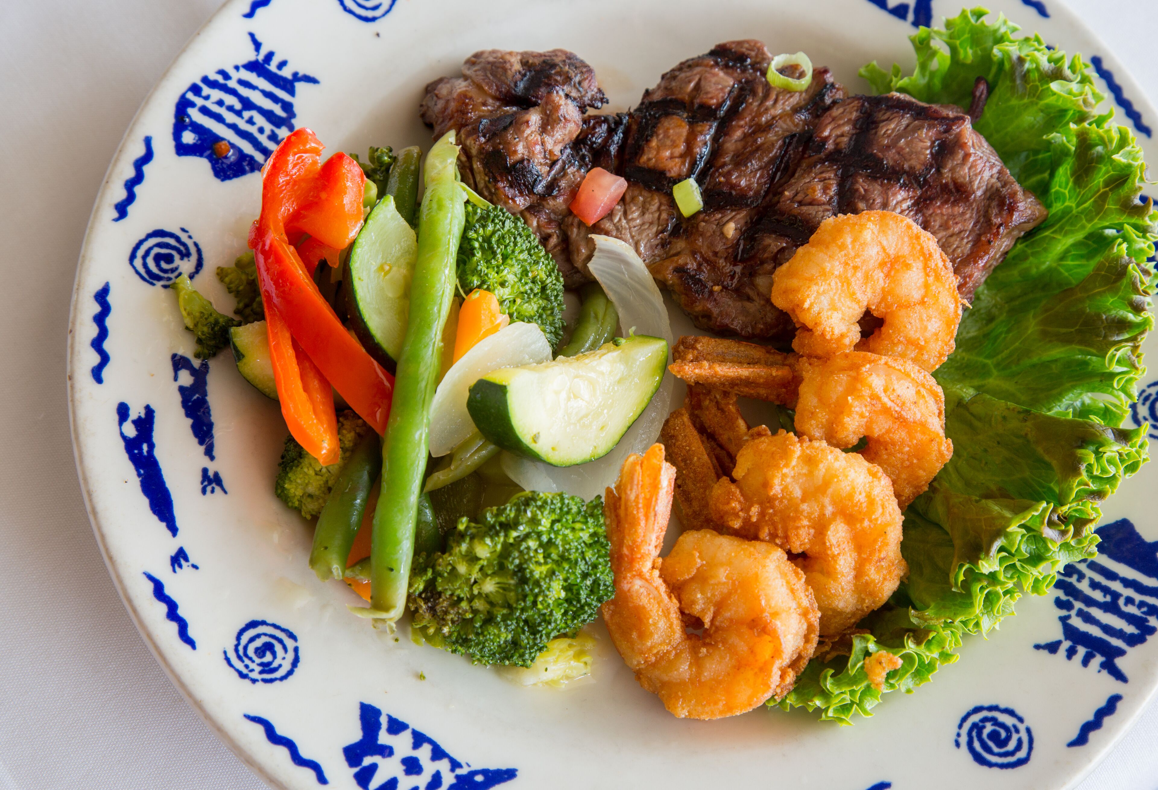 A plate with grilled steak, shrimp, and mixed vegetables.
