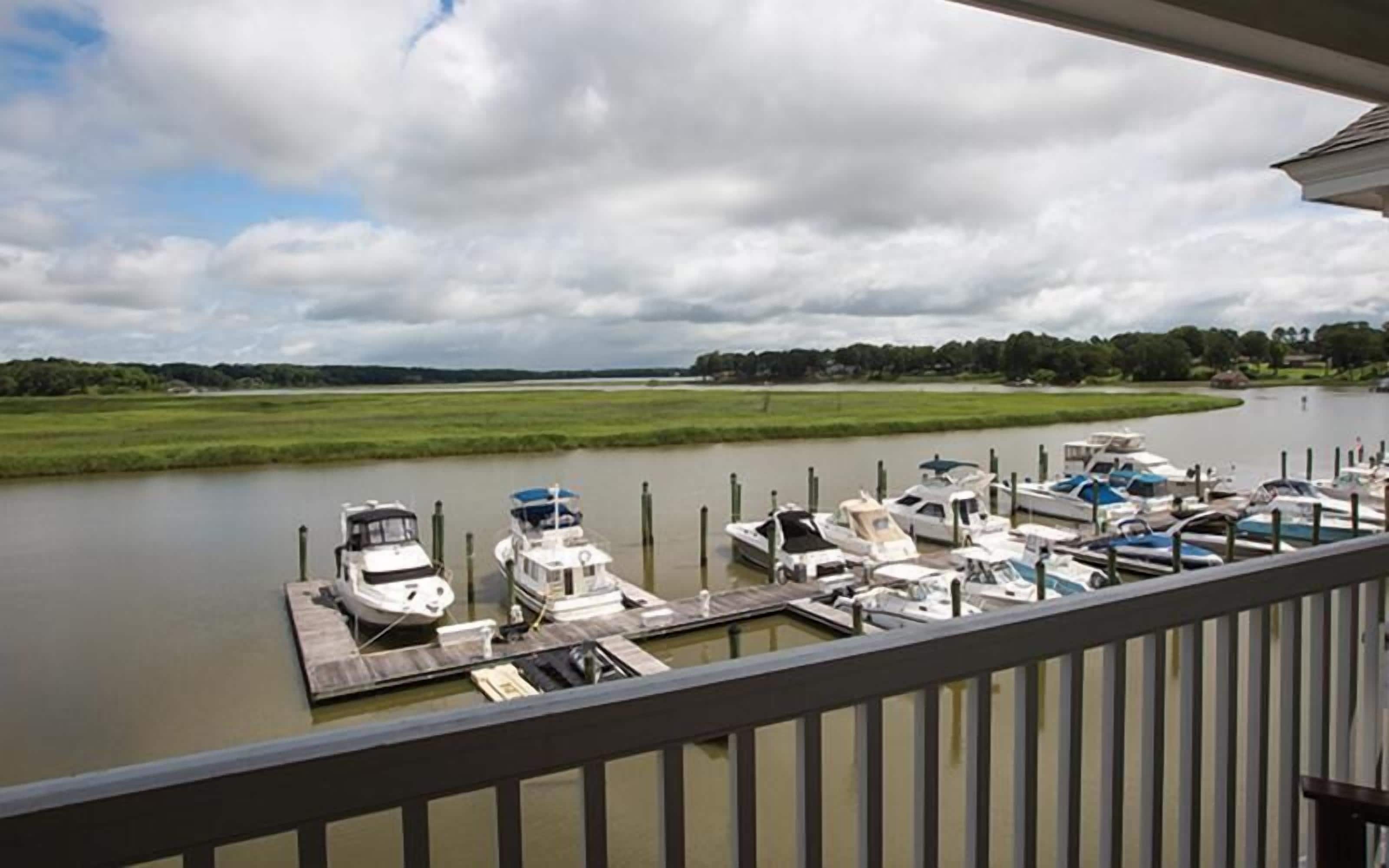 A marina with boats docked, a grassy landscape, and a cloudy sky.