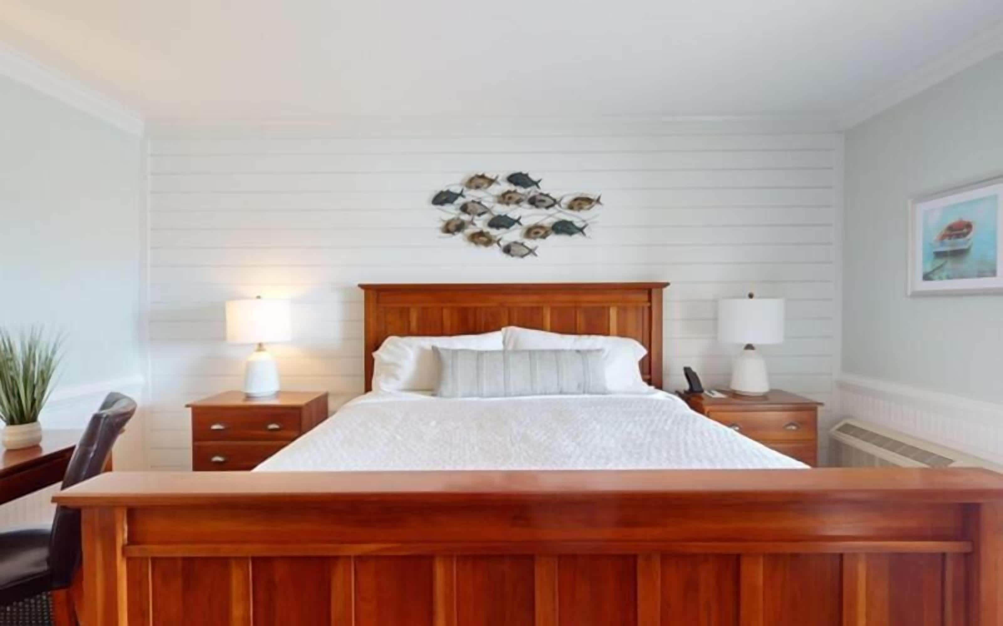 A bedroom with a wooden bed, two bedside tables with lamps, a wall-mounted artwork of fish, and a framed picture on the wall.