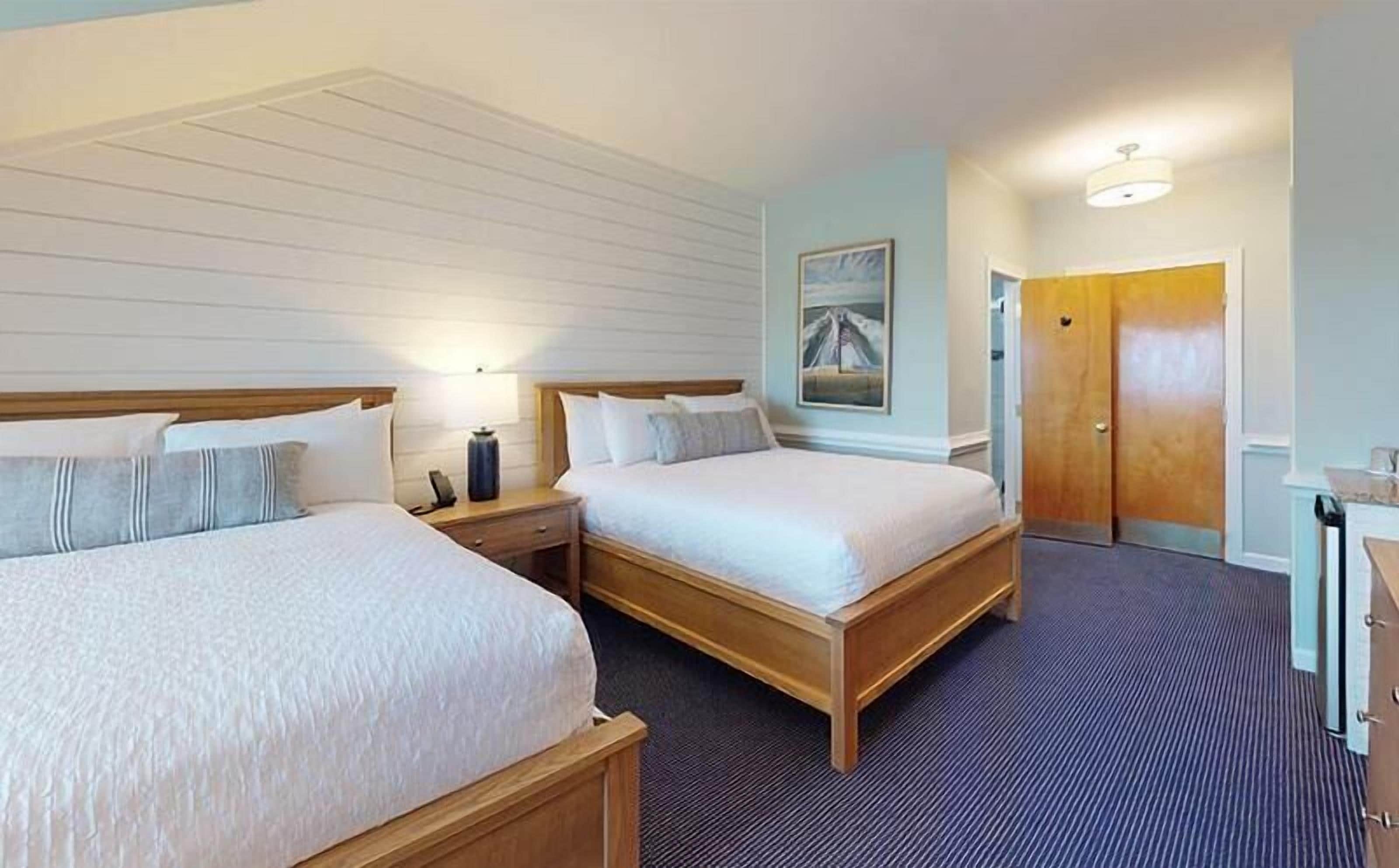 Ett hotellrum med två sängar, ett nattduksbord, en lampa, en tavla och en dörr.