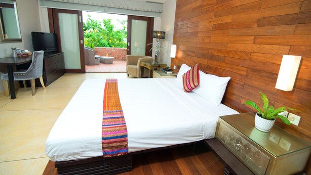 A hotel room with a large bed, a desk with a television, a chair, a small table with a lamp, and a potted plant. - Riverview Cambodia Boutique Hotel (Phnom Penh)