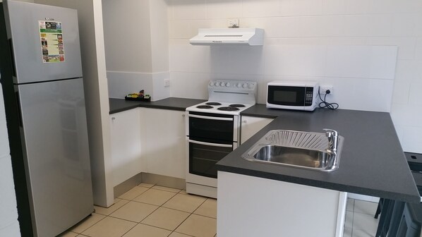 A compact kitchen with a refrigerator, stove, microwave, and sink. - Titree Village Holiday Apartments (Port Douglas)