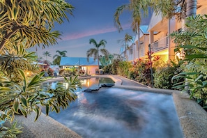 A resort pool area with a clear view of the pool, surrounding palm trees, and a building with balconies. - Titree Village Holiday Apartments (Port Douglas)