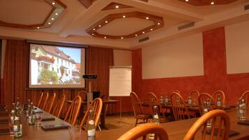 Un salón de conferencias con una larga mesa, sillas, una pantalla de proyector y una pizarra.