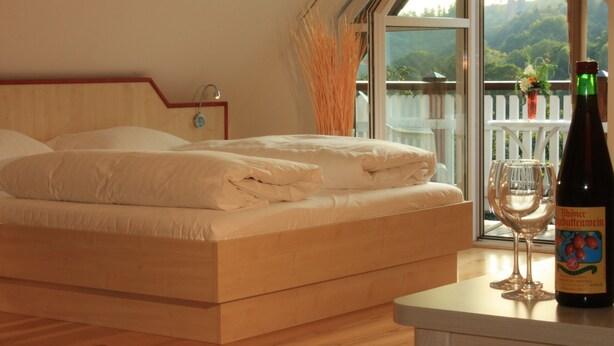 A bedroom with a bed, a bottle of wine, and a glass on a table. - Gasthof zum Biber (Motten)
