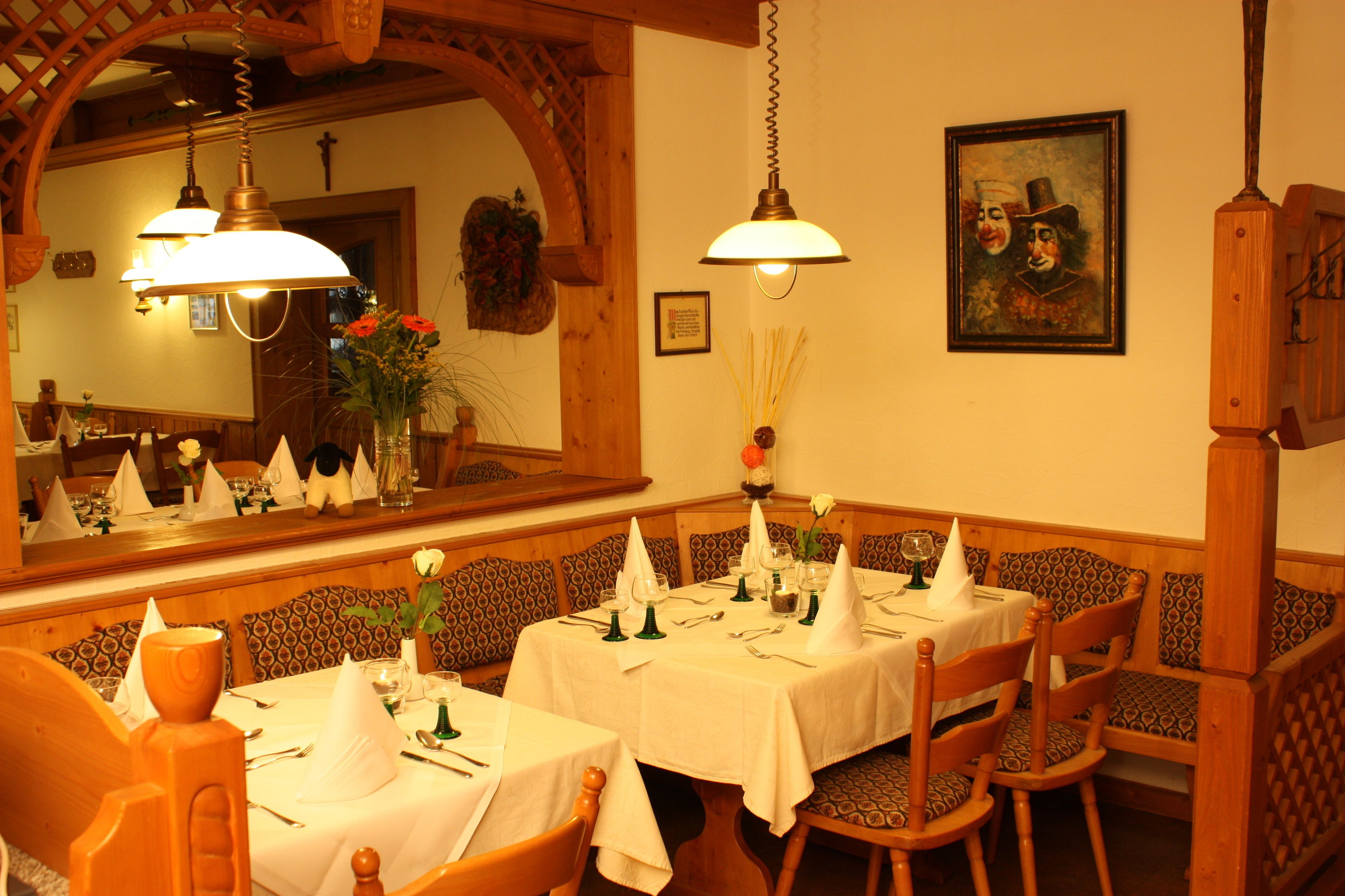 Zona pranzo con sedute in legno, tovaglie bianche e lampade a sospensione.