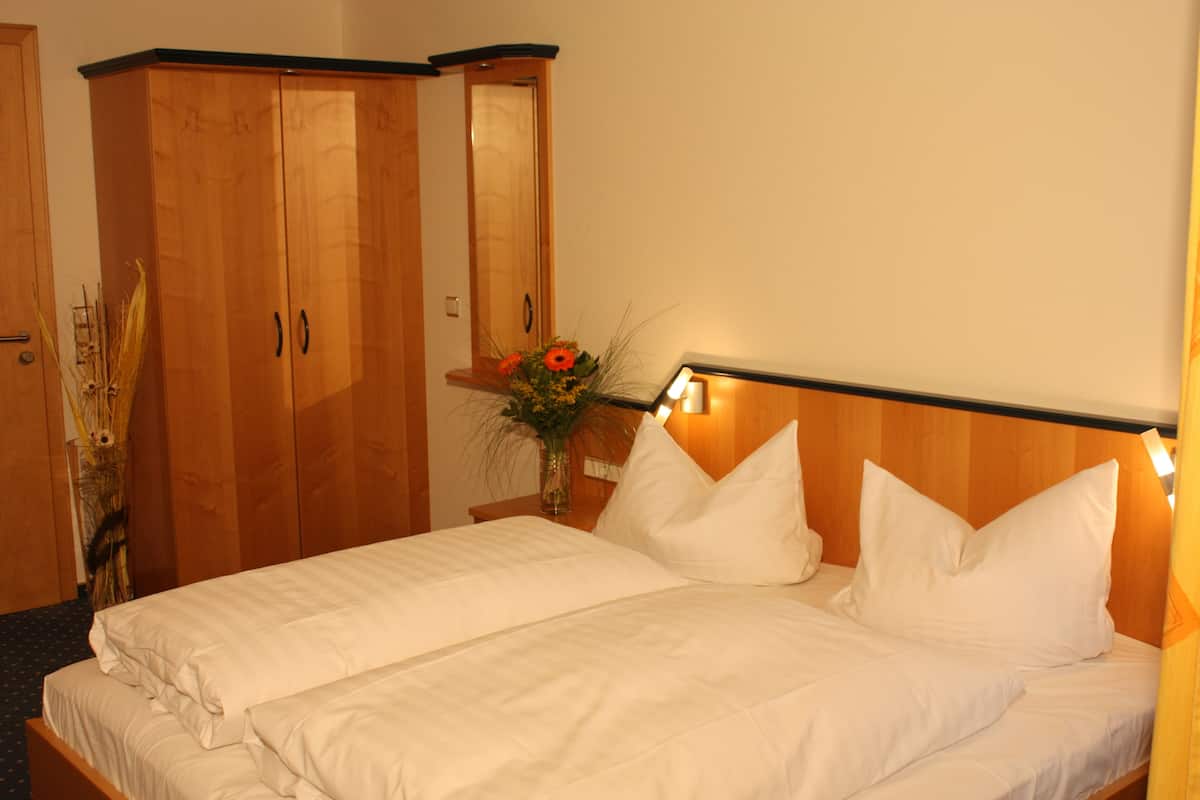 Ein Hotelzimmer mit Bett, Holzschrank und Nachttisch mit Blumenvase.