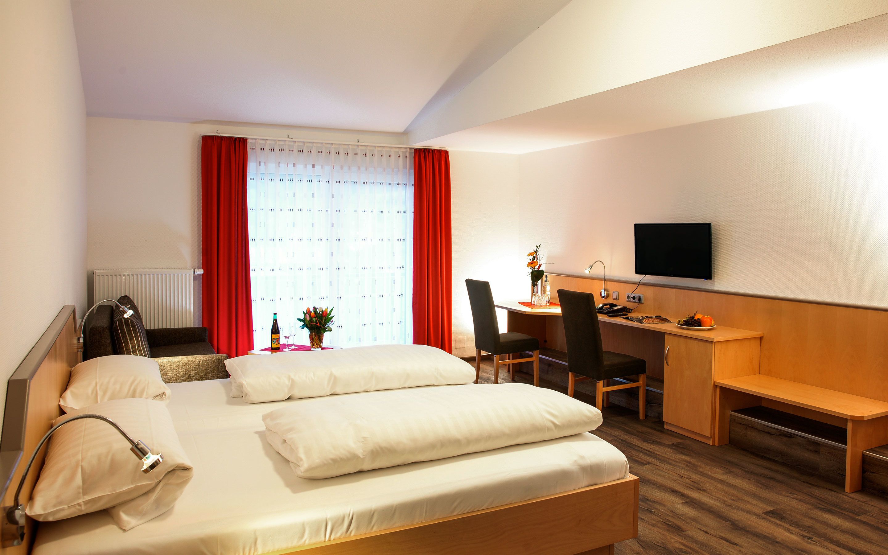 A hotel room with a bed, a desk, a chair, a TV, and a window with curtains.
