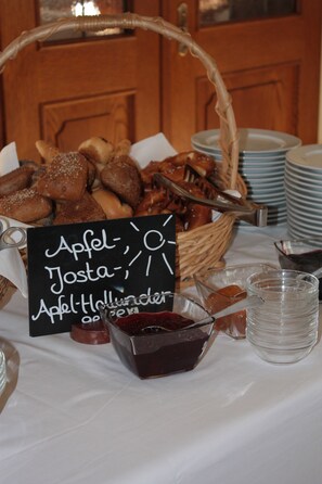 A table with a basket of assorted pastries, a sign with menu items, and a small bowl of jam.