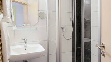 Een moderne badkamer met een douchecabine van glas, een witte wastafel en een spiegel erboven.
