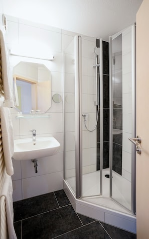 A modern bathroom with a glass-enclosed shower, a white sink, and a mirror above it.