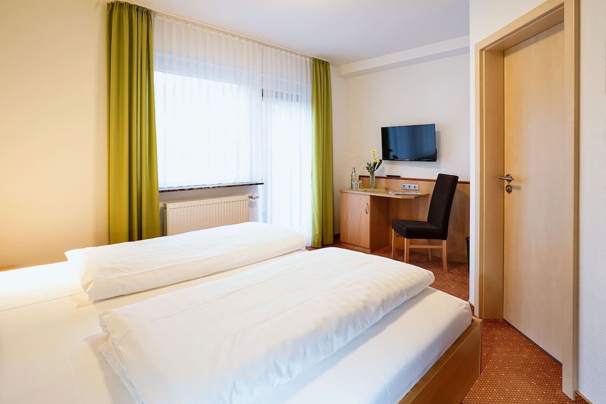 Ein Hotelzimmer mit zwei Betten, einem Schreibtisch mit Stuhl, einem Fernseher und einem Heizkörper.