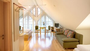 A spacious loft bedroom with a large skylight, a cozy seating area with a sofa and chairs, and a small desk with a computer. - Gasthof zum Biber (Motten)