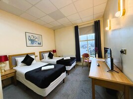 Habitación de hotel con dos camas, un escritorio, una silla, una ventana con cortinas y un cuadro en la pared.