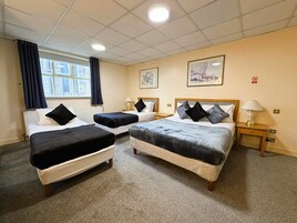 A hotel room with two single beds, a double bed, and a small table with a lamp.