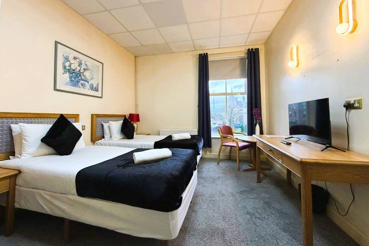 A hotel room with two beds, a desk, a TV, and a window with a city view.