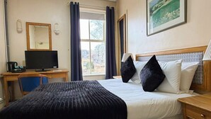A hotel room with a bed, a desk with a computer, a chair, and a window with curtains. - Throstles Nest Hotel (Liverpool)