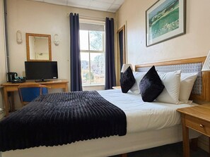 A hotel room with a bed, a desk with a computer, a chair, and a window with curtains. - Throstles Nest Hotel (Liverpool)