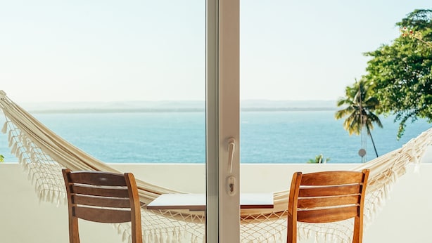 A hammock chair and table setup with a view of the ocean. - Hotel Pousada Natureza (Cairu)