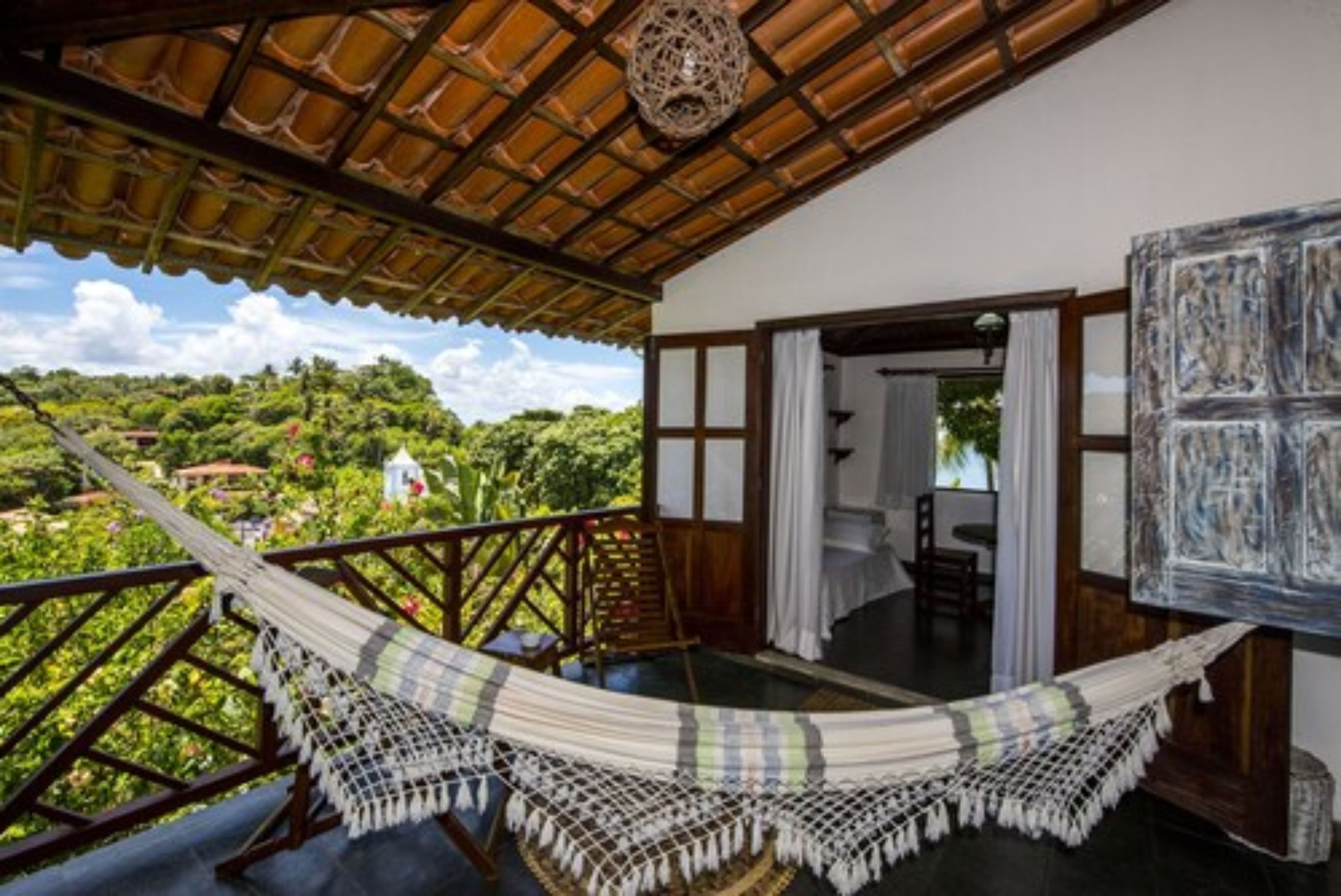 A room with a hammock, a painting, and a view of greenery.