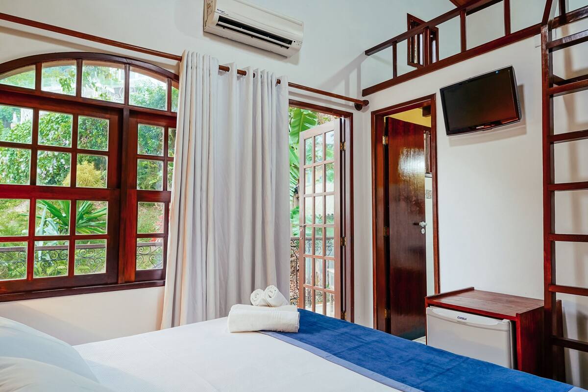 Une chambre d’hôtel avec un lit, un petit bureau, une télévision et une fenêtre avec des rideaux.