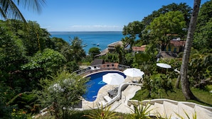 A pool surrounded by lush greenery and a view of the sea. - Hotel Pousada Natureza (Cairu)