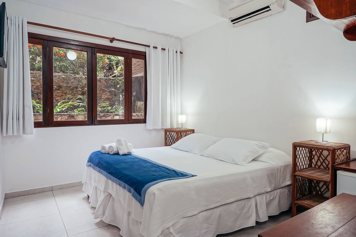 Une chambre à coucher avec un lit, une table de chevet, une lampe et une vue sur l’extérieur par une fenêtre.