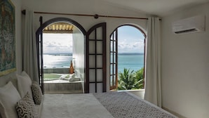 A hotel room with a large bed, two windows with views of the sea, a small balcony, and an air conditioning unit. - Hotel Pousada Natureza (Cairu)