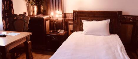 Habitación de hotel con cama de madera, un escritorio, una silla, una mesita de noche con lámpara y un jarrón con flores.