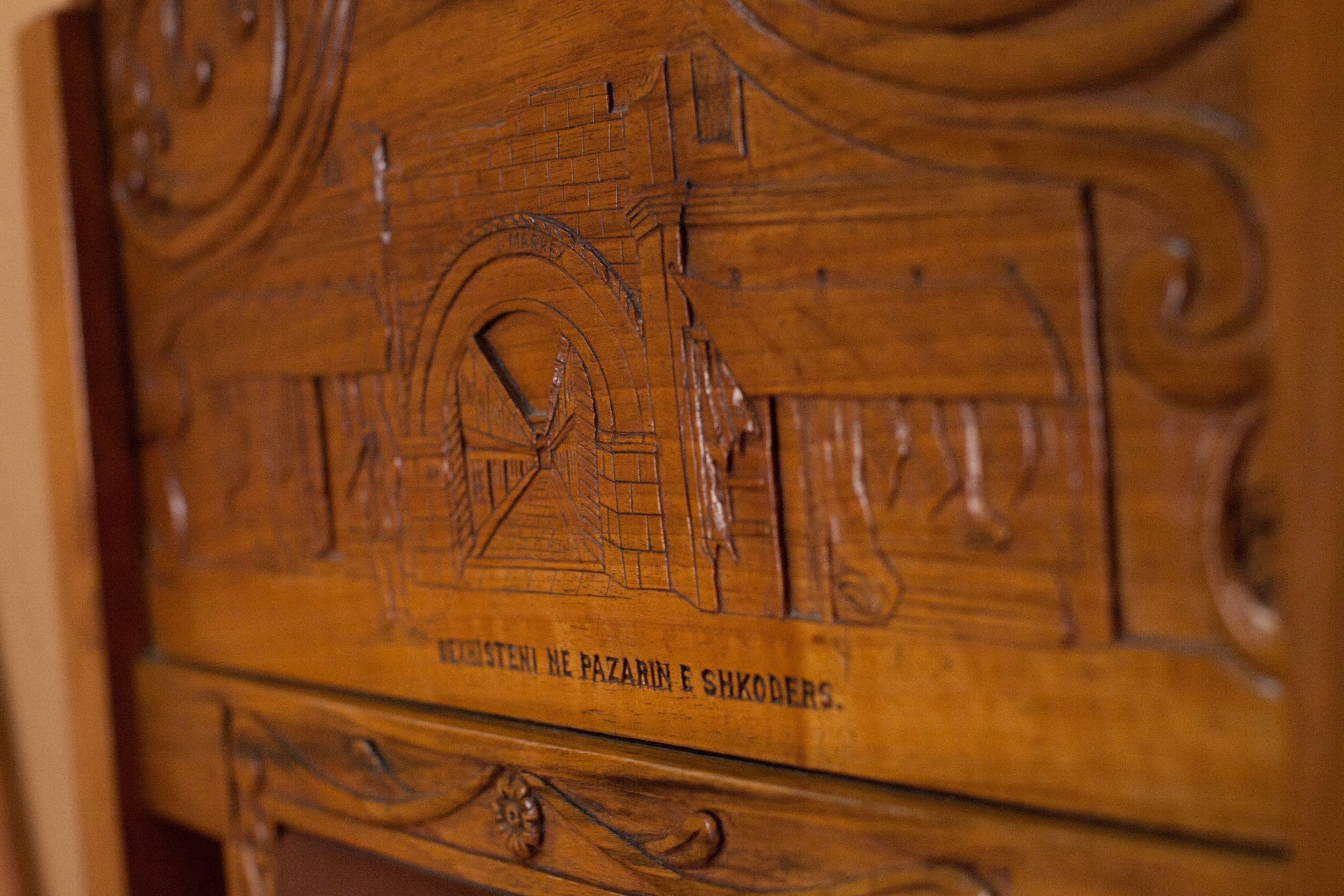 A wooden carved panel with architectural designs and the inscription "MESTENI NE PAZARIN E SHKODERS."