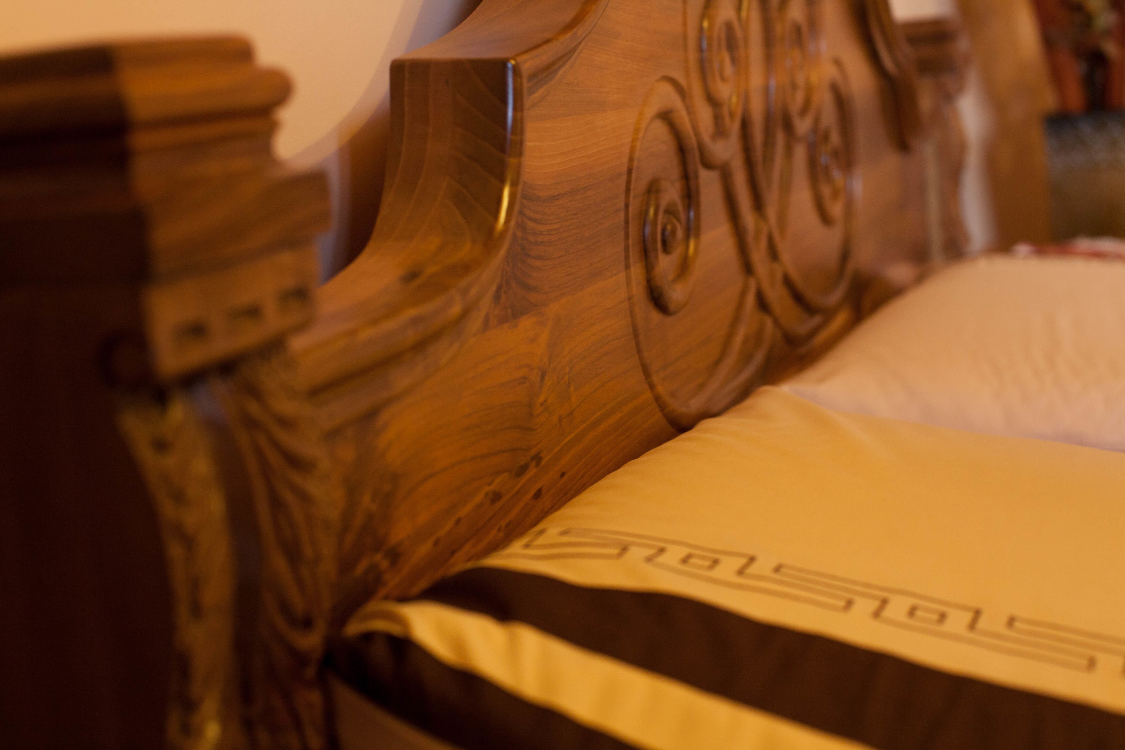 Cabecera de madera con tallas intrincadas y un almohadón con logotipo visible.