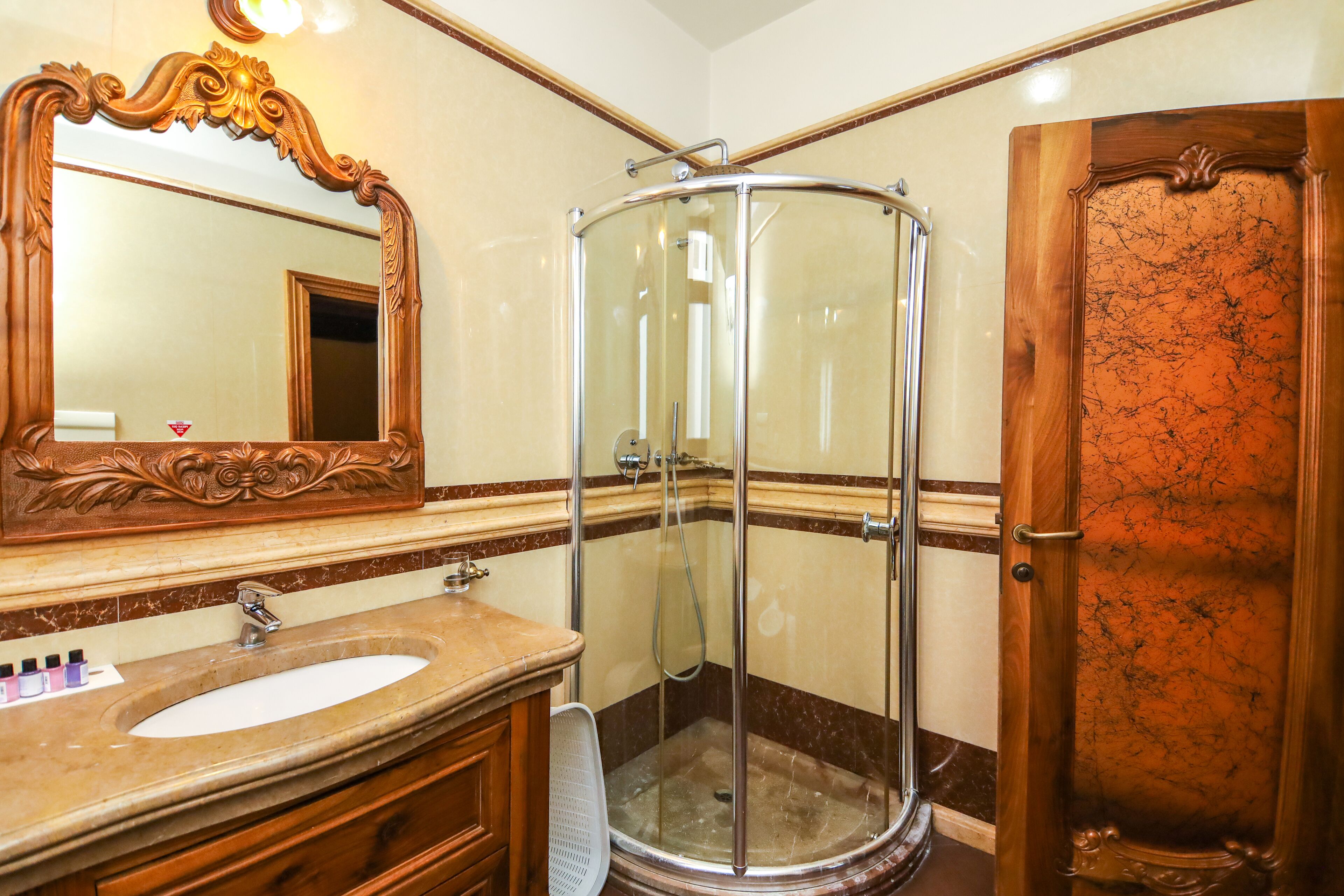 A bathroom with a marble sink, a glass shower enclosure, and a wooden door.