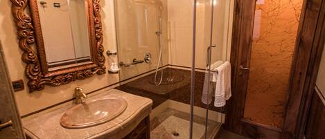A bathroom with a marble sink, a glass shower enclosure, and a wooden door.