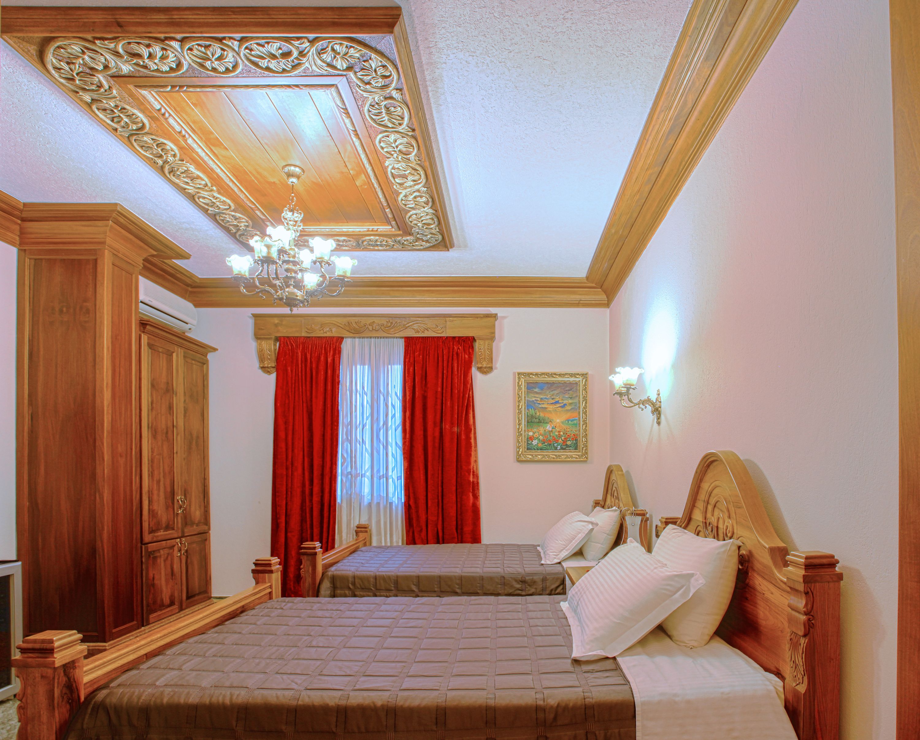A bedroom with two beds, wooden headboards, a chandelier, a painting, and a red curtain.