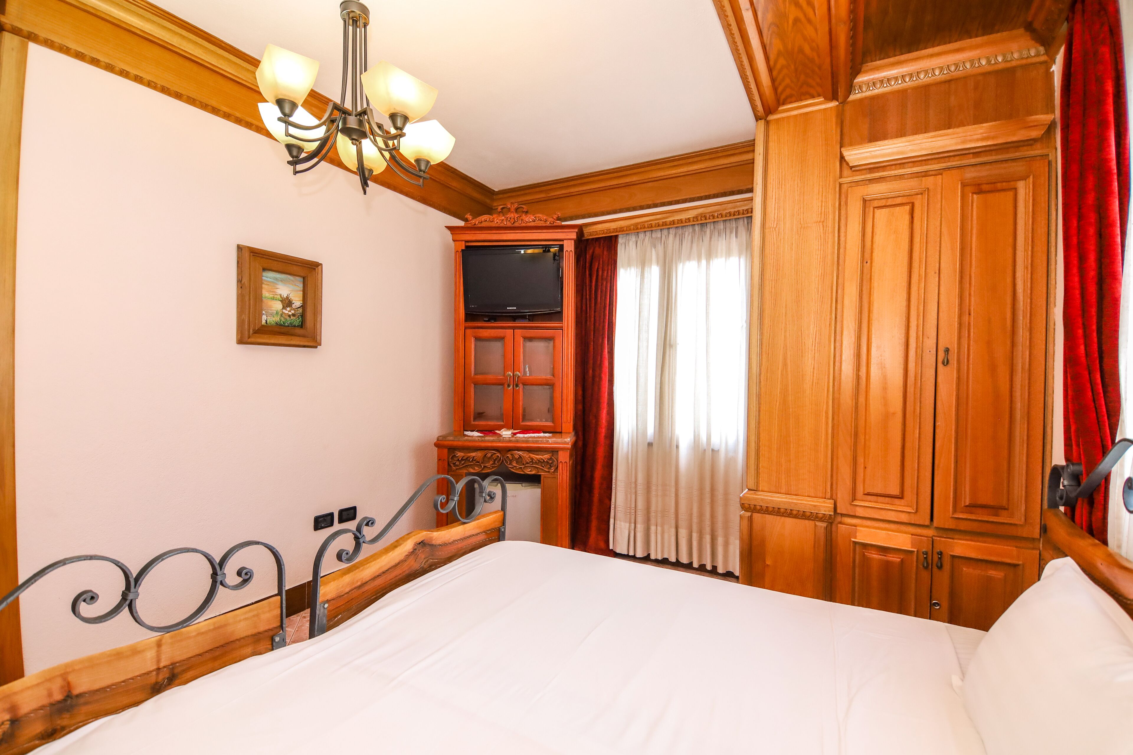 Una habitación de hotel con estructura de cama de madera, un televisor en un mueble bajo y un amplio armario.