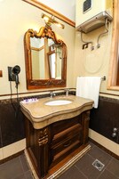 Un baño con lavamanos de mármol, tocador de madera y un espejo grande y decorativo.