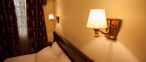A hotel room with a bed, a wall-mounted lamp, and an air conditioning unit.
