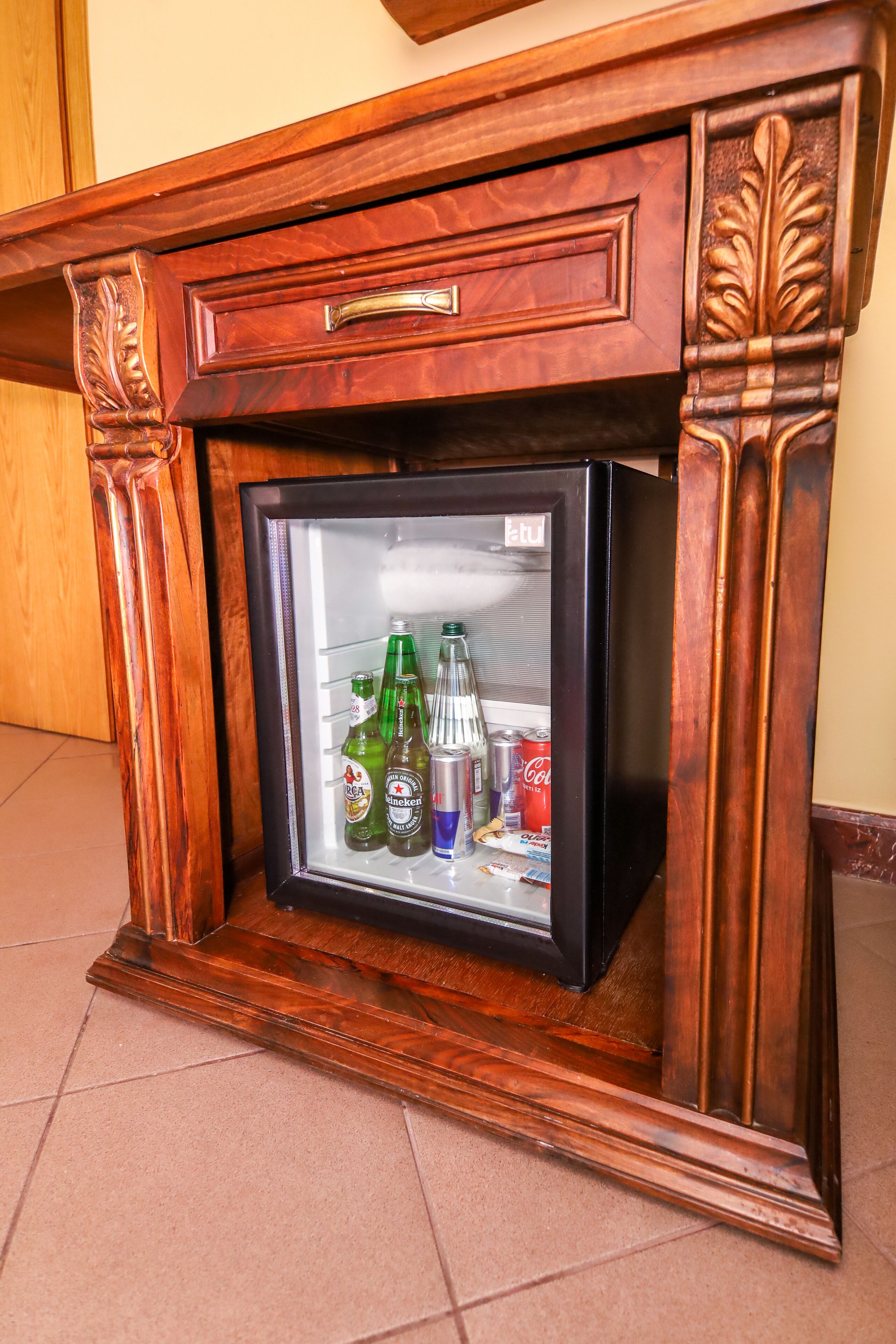 A wooden cabinet with a built-in mini-fridge containing various beverages.