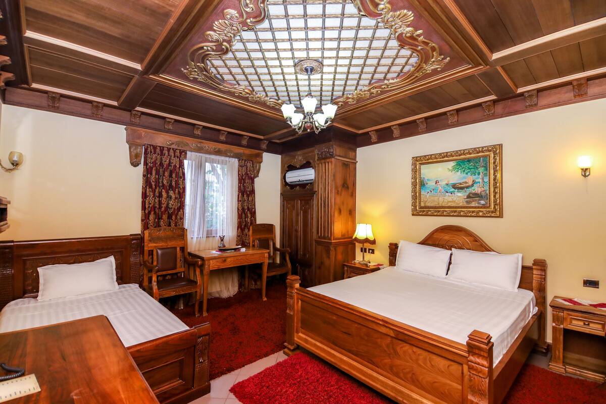 A hotel room with two wooden beds, a desk, a chair, a red carpet, and a chandelier.