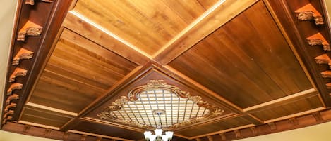 A room with a wooden ceiling, a chandelier, a painting, and a wall-mounted light fixture.