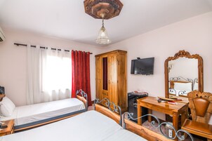 A hotel room with two beds, a wooden wardrobe, a desk with a chair, a television, and a large mirror.