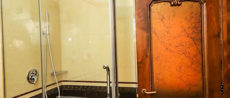 A glass-enclosed shower stall with a towel hanging on the door handle, a wooden door with a marble-like pattern, and a tiled floor.