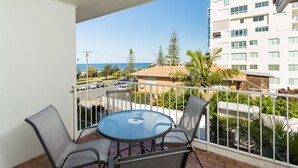 A balcony with a round table and two chairs, overlooking a residential area with a view of the ocean and a tall building. - Burleigh Point Holiday Apartments (Miami)