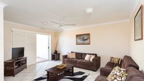 A living room with a sofa set, a television, a ceiling fan, and a zebra-patterned rug. - Burleigh Point Holiday Apartments (Miami)