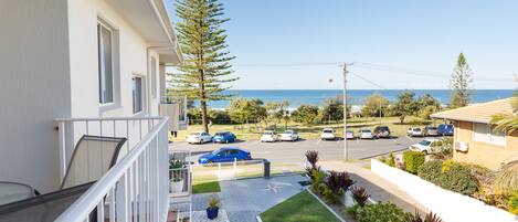 A residential area with a balcony overlooking a street with parked cars and a clear view of the ocean.