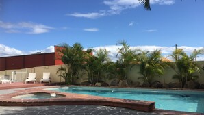 A swimming pool with a stone deck, palm trees, and a red building in the background. - Burleigh Point Holiday Apartments (Miami)