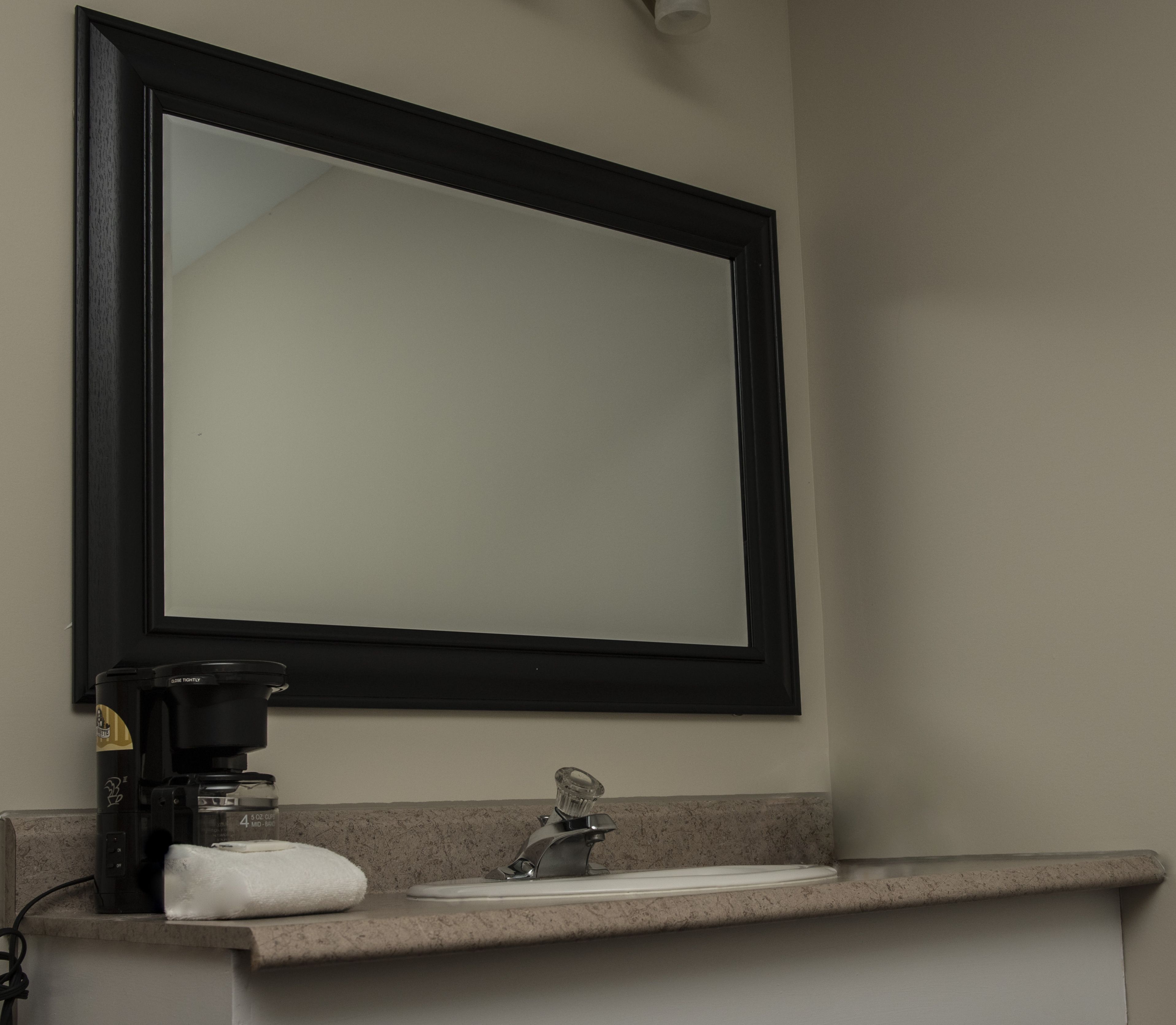 A bathroom with a large mirror, a coffee maker, and a towel on the counter.