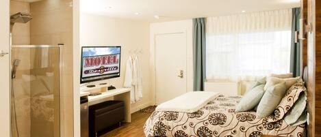 Une chambre d’hôtel avec un lit, un bureau, une télévision et une douche.