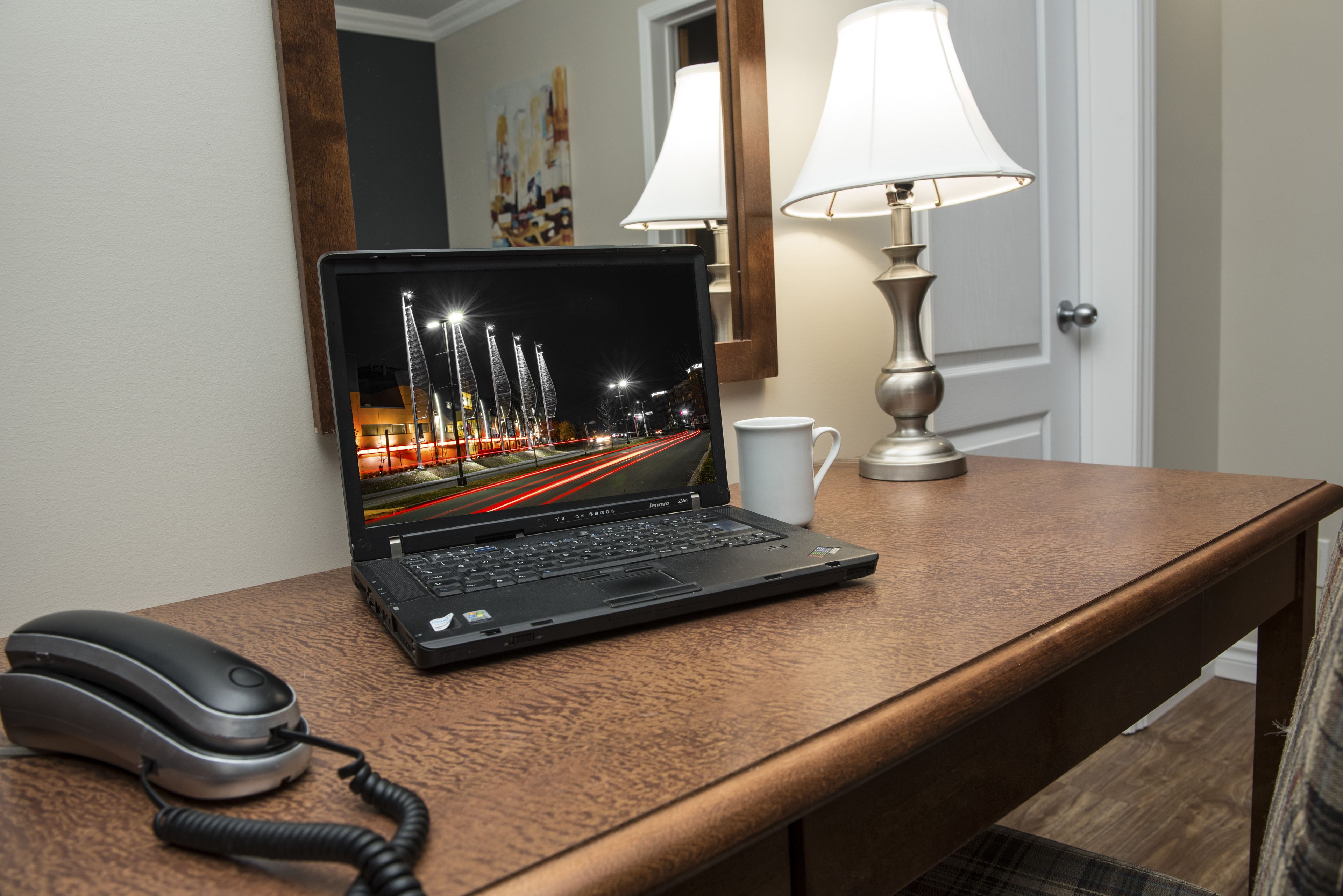 Un ordinateur portable sur un bureau en bois, avec une lampe et un téléphone.