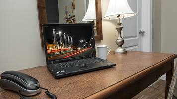Un ordinateur portable sur un bureau en bois, avec une lampe et un téléphone.
